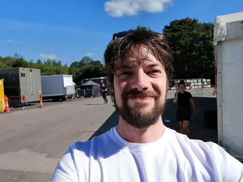 A selfie of Mat in a white t-shirt taken outside in a film studio lot with blue sky above